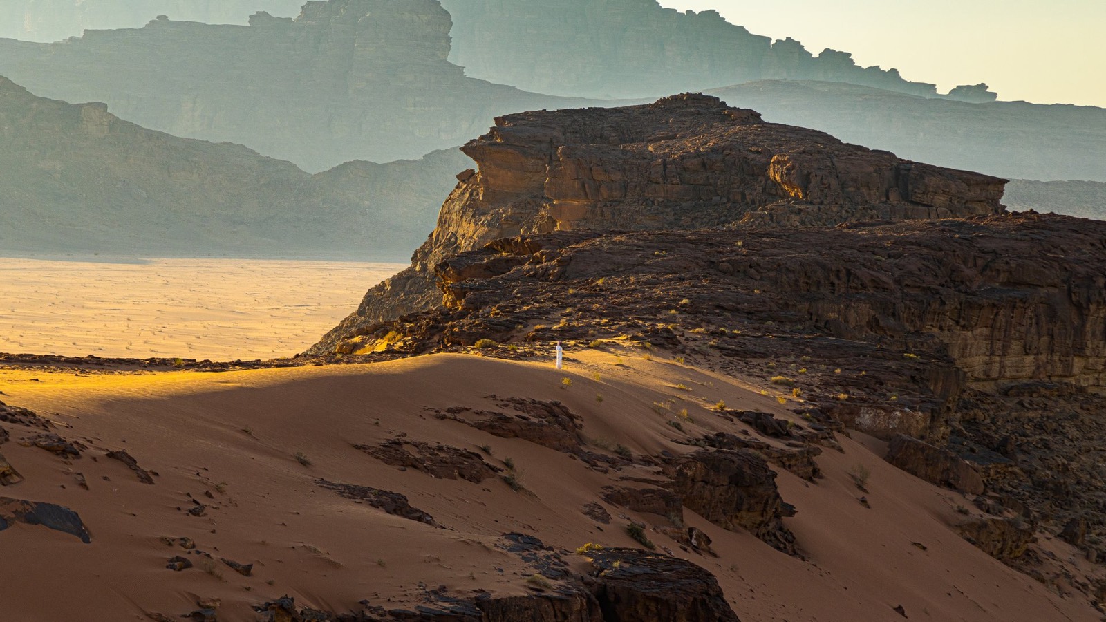 A lone figure in white standing on a desert dune